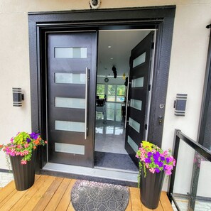 A modern entrance with a black door featuring horizontal panels and a glass panel. There are two flower planters on either side of the door.