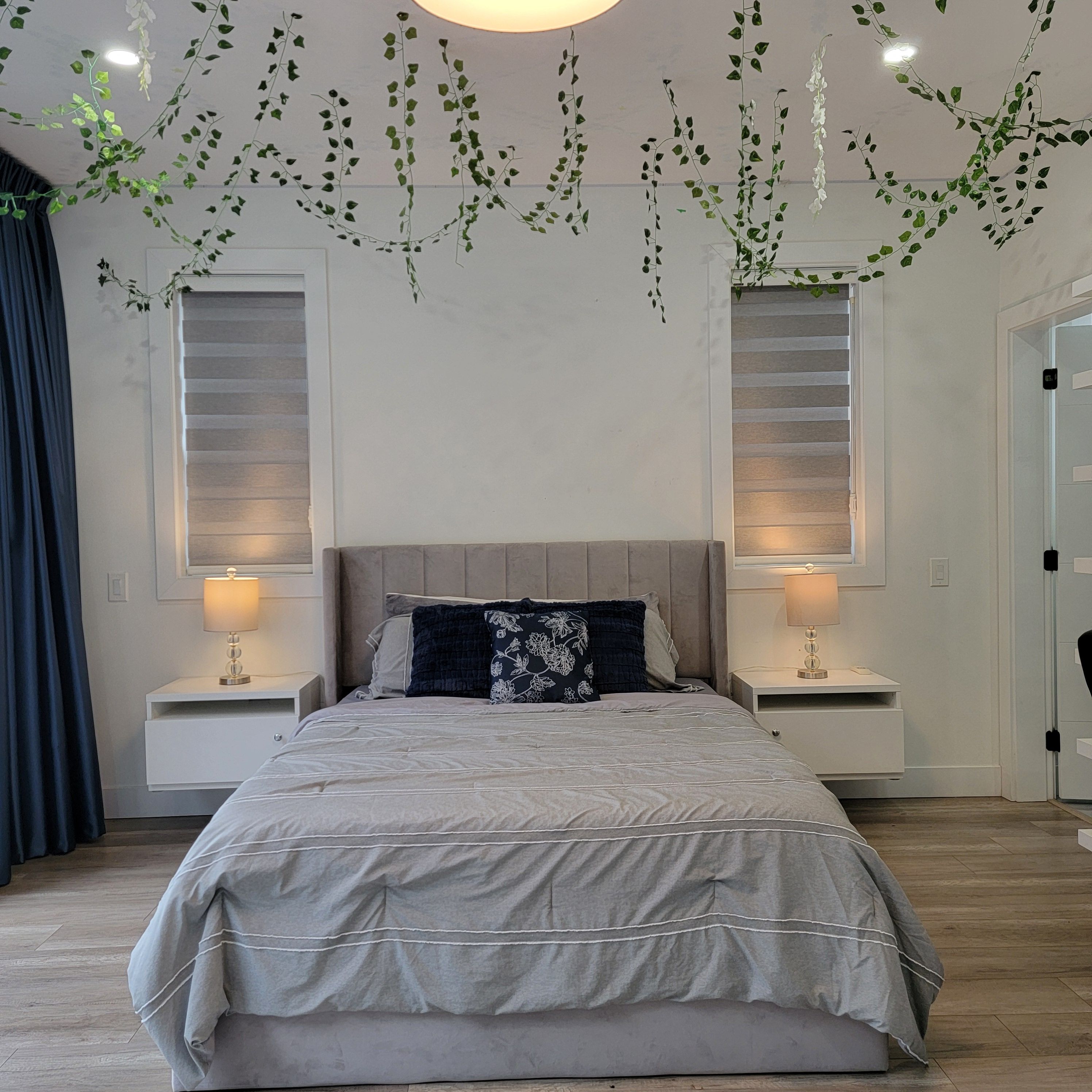 A bedroom with a large bed, two bedside tables, a headboard, and hanging plants.