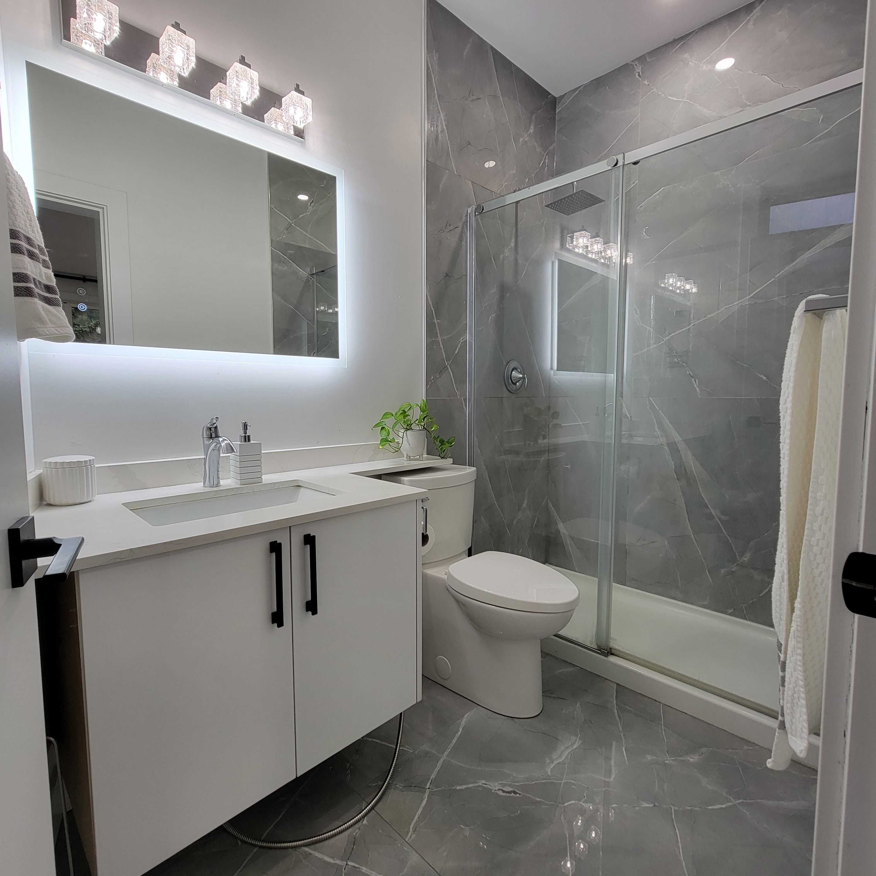 A modern bathroom with a glass-enclosed shower, a white sink with a mirror above, and a toilet.