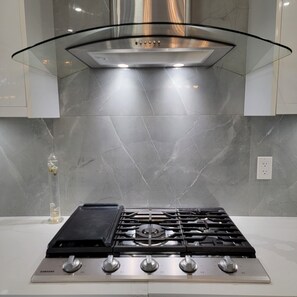 A kitchen with a stainless steel range hood, a gas stove, and a marble backsplash. - Nature's Lodge on the River (Hope)