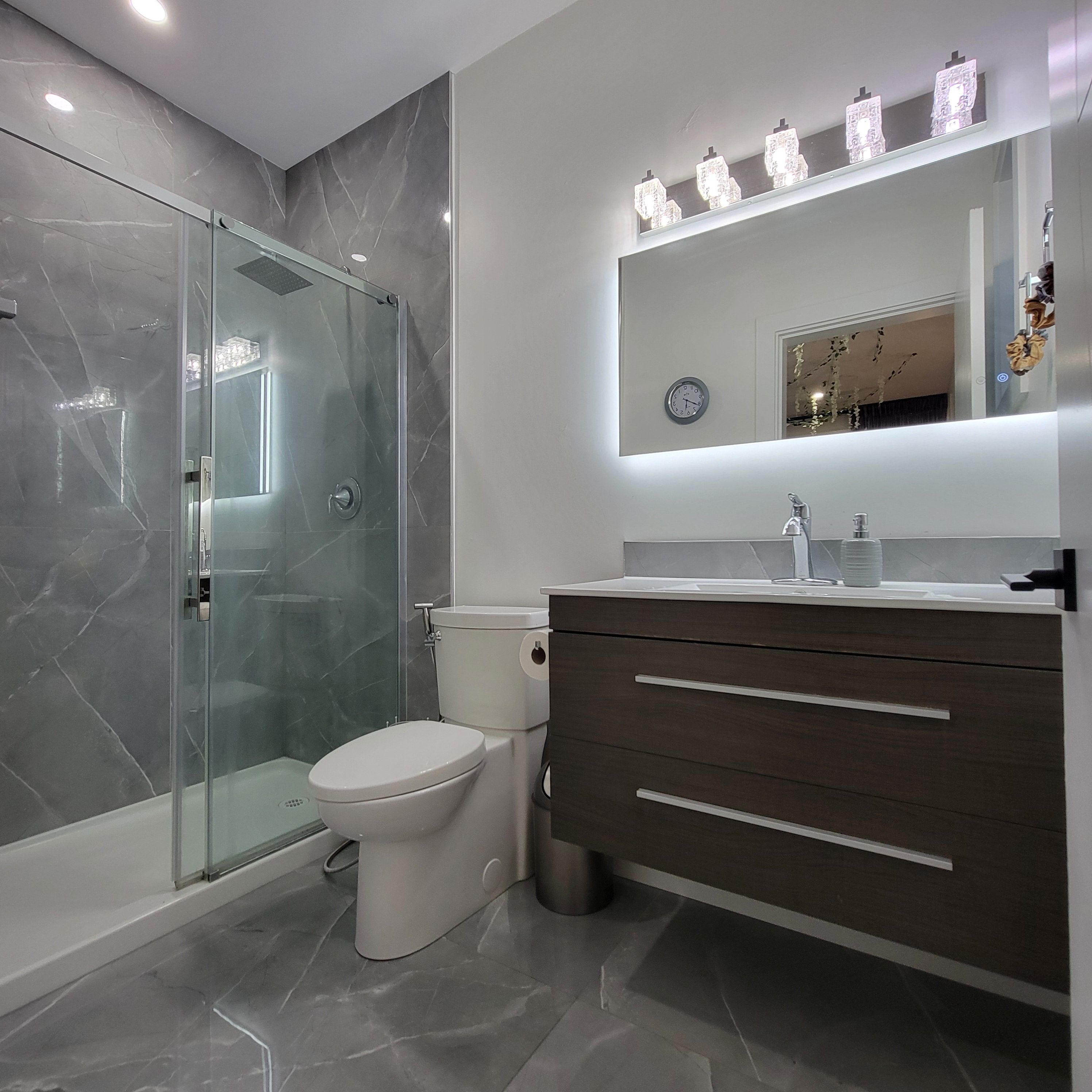 Un baño moderno con ducha envuelta en vidrio, inodoro y tocador con cajones.