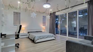 A modern bedroom with a bed, a desk, and a chair. There is a large window with curtains and a view of the outside.
