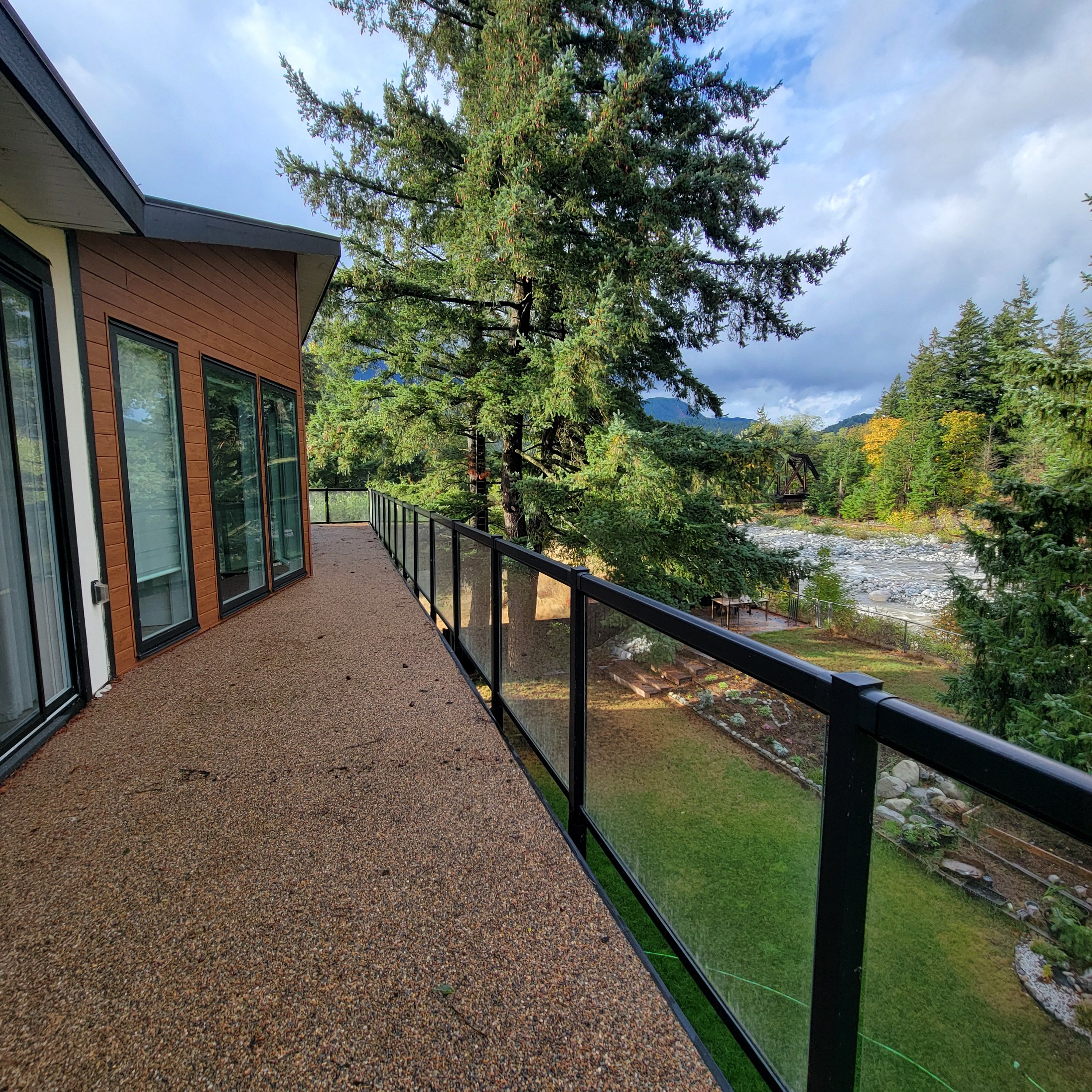 A balcony with a gravel floor, overlooking a garden with trees and a river.