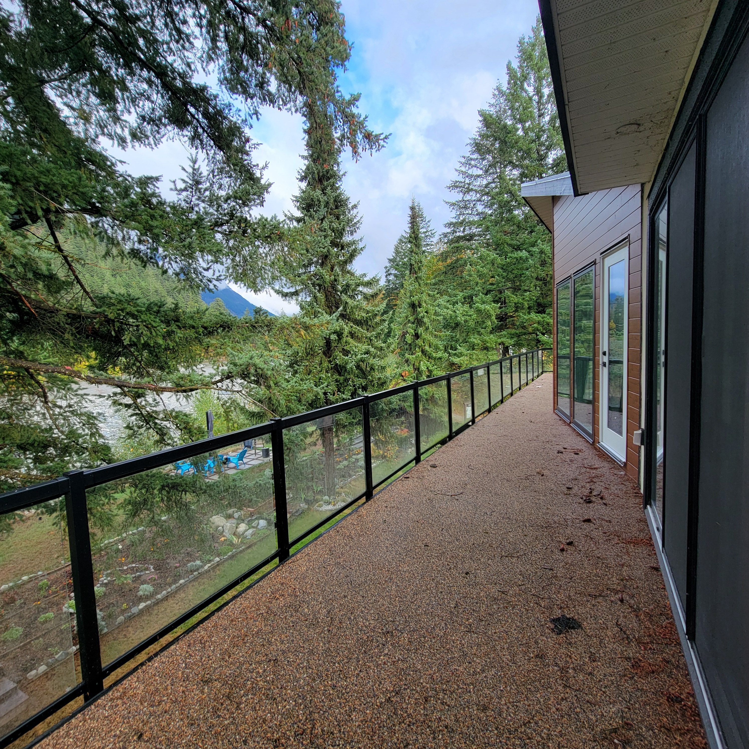 A balcony with a gravel floor and a glass railing overlooking a forested area with a mountain in the distance.