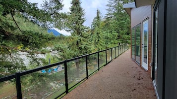 A balcony with a gravel floor and a glass railing overlooking a forested area with a mountain in the distance.