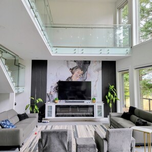 A modern living room with a large flat-screen TV, a glass staircase, and a marble wall.