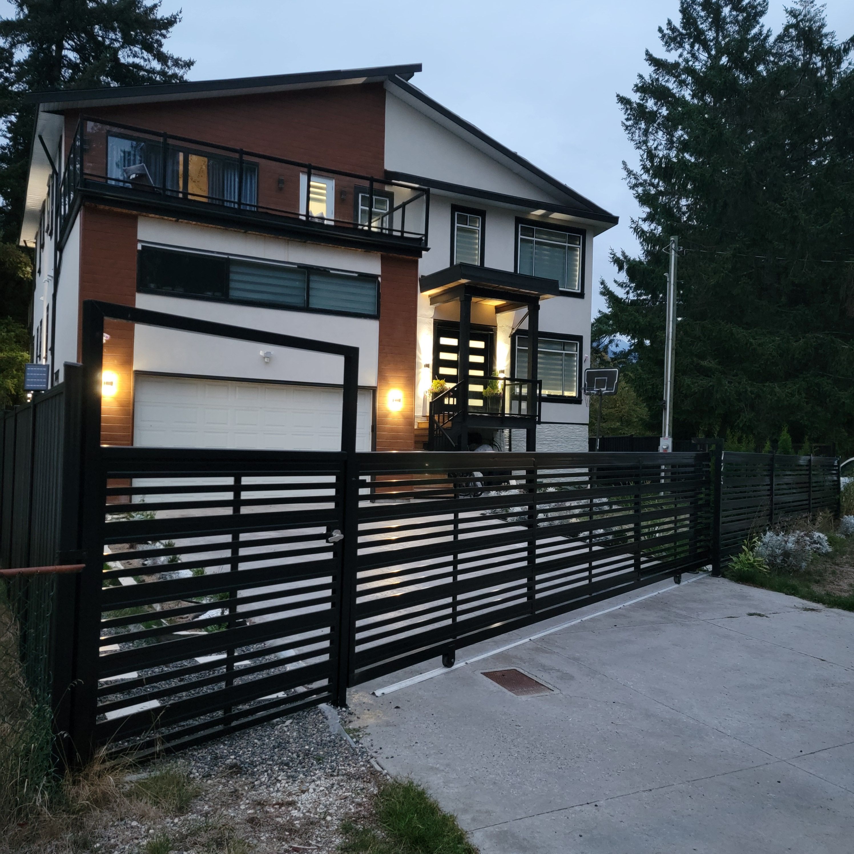 Una casa moderna a due piani con garage, un balcone e una recinzione nera.