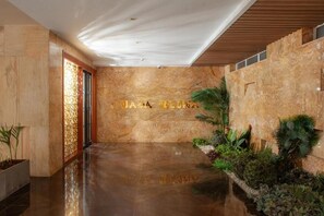 Un vestíbulo con piso pulido, pared de piedra con inscripción dorada y un pequeño jardín interior con diversas plantas.
