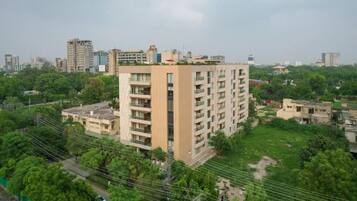 A multi-story residential building with a flat roof, surrounded by greenery and other buildings in the background.