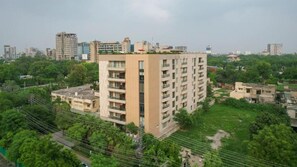Un edificio residencial de varios pisos con techo plano, rodeado de vegetación y otros edificios al fondo.