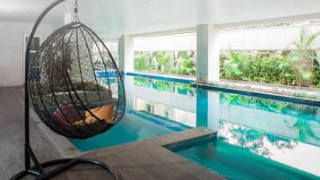 A hanging chair by a pool with a view of the pool and greenery.