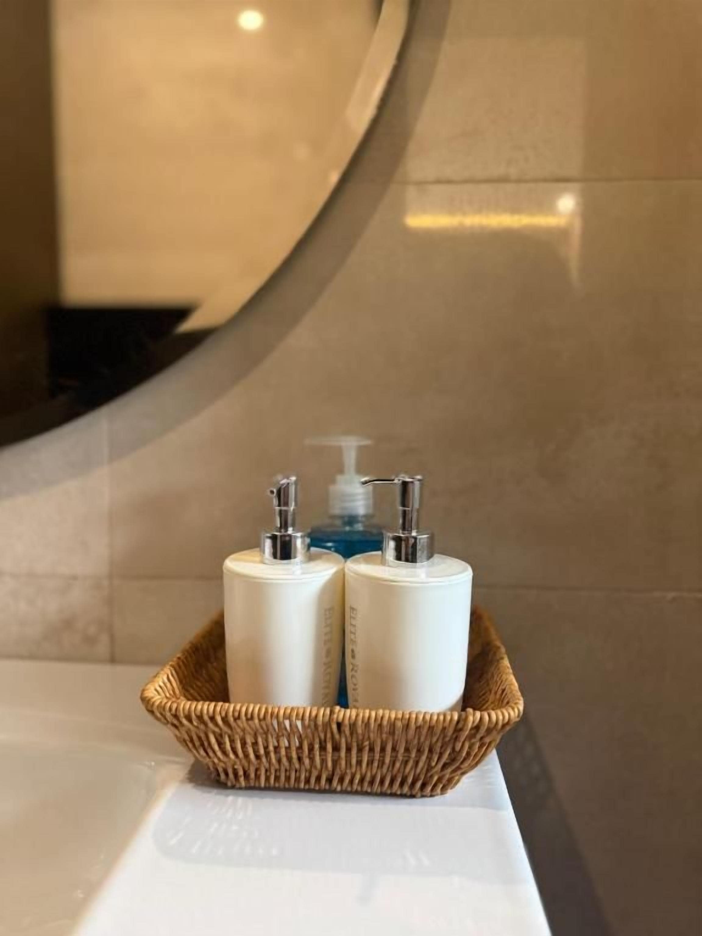 A bathroom with a white sink, a wicker basket containing two white bottles, and a mirror reflecting the wall.