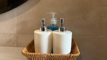 A bathroom with a white sink, a wicker basket containing two white bottles, and a mirror reflecting the wall.
