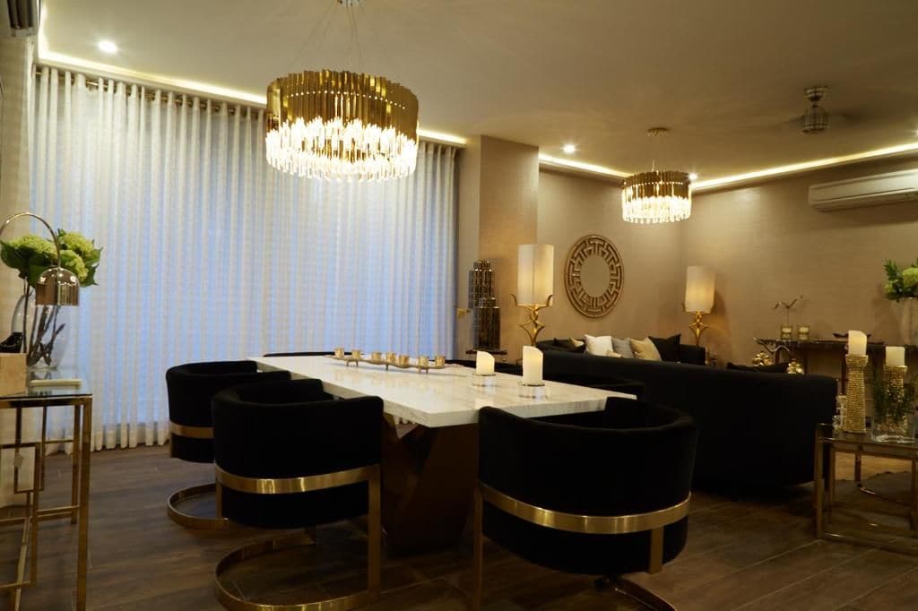 Un espace repas moderne avec une grande table, des chaises à revêtement noir et deux lustres.