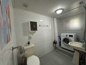 A bathroom with a toilet, washing machine, and sink.