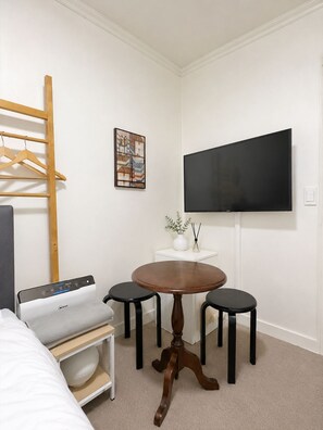 A hotel room with a bed, a desk with a printer, a round table with two chairs, a TV on the wall, and a painting on the wall.