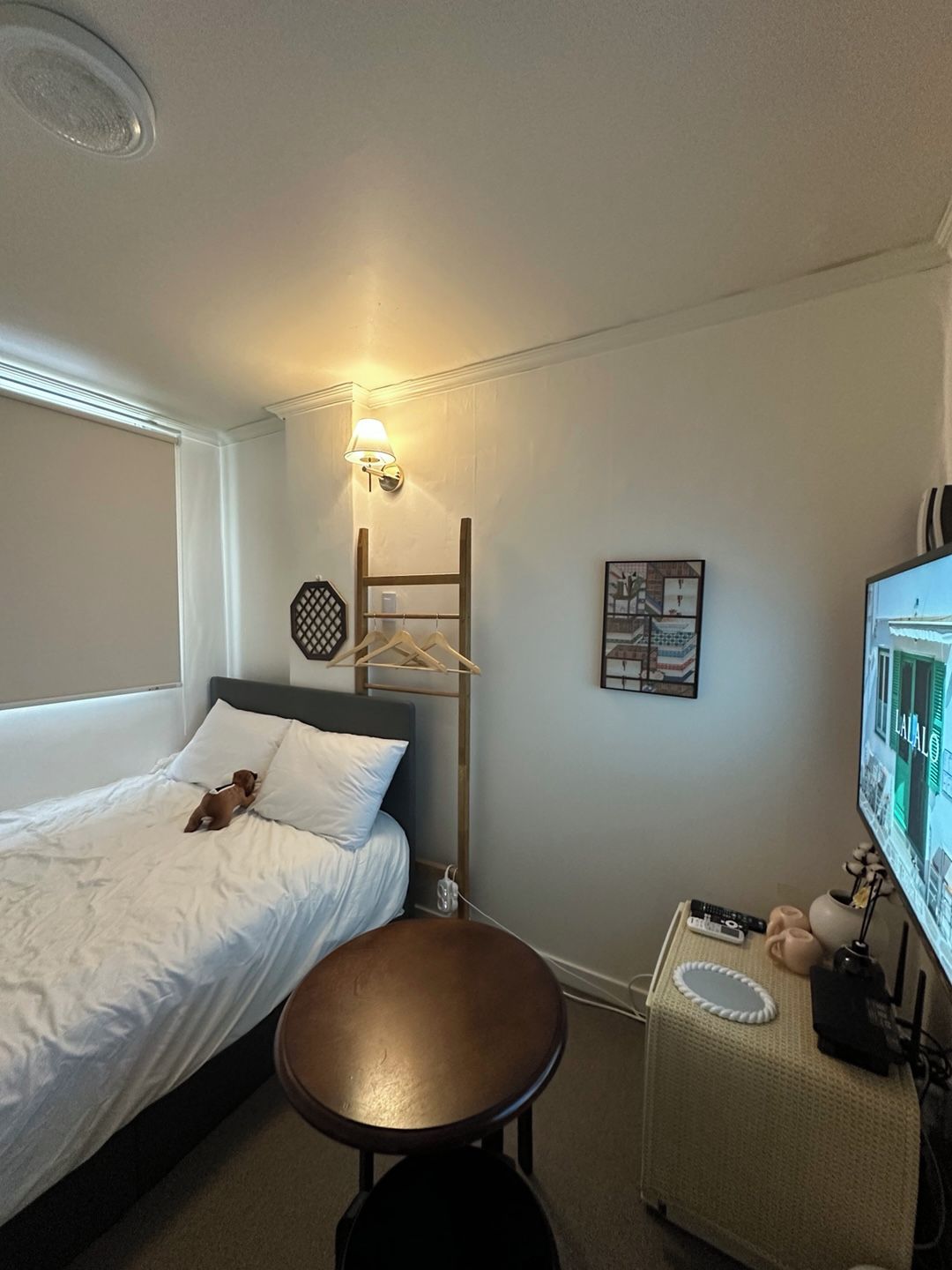 A hotel room with a bed, a small table, a wall-mounted TV, and a hanging light fixture.