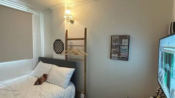 A hotel room with a bed, a small table, a wall-mounted TV, and a hanging light fixture.