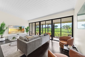 A modern living room with a grey sofa, a brown leather chair, and a large window offering a view of a green landscape. - Fantastic 2-bedroom condo in soothing Palm Beach Gardens (Palm Beach Gardens)