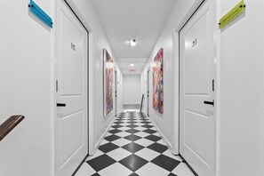 Un couloir avec des portes blanches, un sol à carreaux noirs et blancs, et des œuvres d’art colorées accrochées aux murs.
