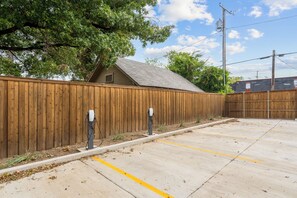 A parking area with a wooden fence, a concrete surface, and a building with a sloped roof in the background. - Chic 1 BR Art Deco-Bishop Arts-Nr Downtown Dallas (Dallas)