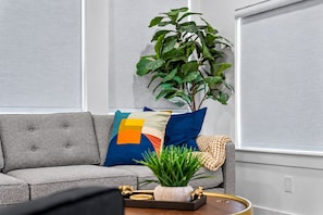 A grey sofa with a geometric patterned pillow, a potted plant, and a small table with a tray. - Chic 1 BR Art Deco-Bishop Arts-Nr Downtown Dallas (Dallas)