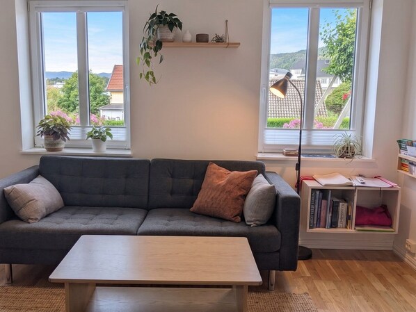 A living room with a grey sofa, a wooden coffee table, and a bookshelf with books and decorative items.