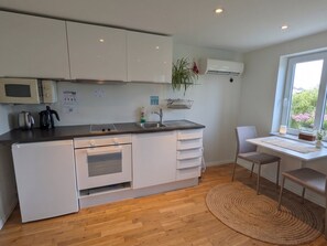 A compact kitchen with white cabinets, a microwave, a kettle, and a sink. There's a window with a view of greenery outside.