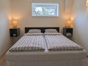 A double bed with striped bedding, two bedside tables with lamps, a window with a view, and a small shelf with books. - A private apartment, all to yourself. (Møre og Romsdal)