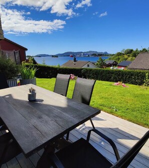 Um deck de madeira com mesa e cadeiras, com vista para um corpo d'água e colinas.