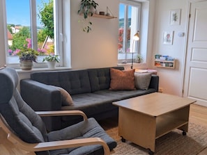 A modern living room with a grey sofa, a wooden coffee table, and a chair. There are potted plants on the windowsill and a bookshelf with books and decorative items. - A private apartment, all to yourself. (Møre og Romsdal)