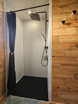 A shower area with a showerhead, curtain, and a towel rack.
