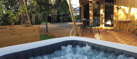 Una terraza de madera con un jacuzzi, mobiliario exterior y una zona de estar cubierta.