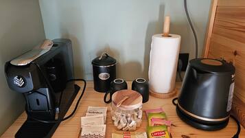 A coffee station with a coffee maker, a kettle, a tea kettle, a jar of biscotti, and packets of tea and biscotti.