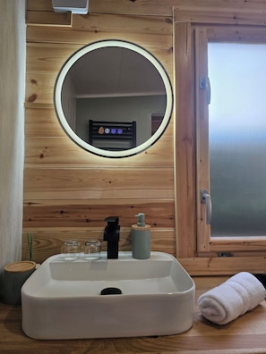 A bathroom with a round mirror, a sink, a soap dispenser, and a towel.