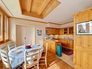 A compact kitchen with wooden cabinets, a dining area with a table set for four, and a small island with a sink. - Le Chamois d'Or A303 by Interhome (Crans-Montana)