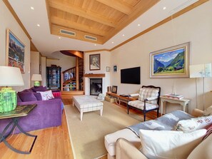 A spacious living room with a fireplace, wooden ceiling, and a large painting on the wall. - Le Chamois d'Or A303 by Interhome (Crans-Montana)