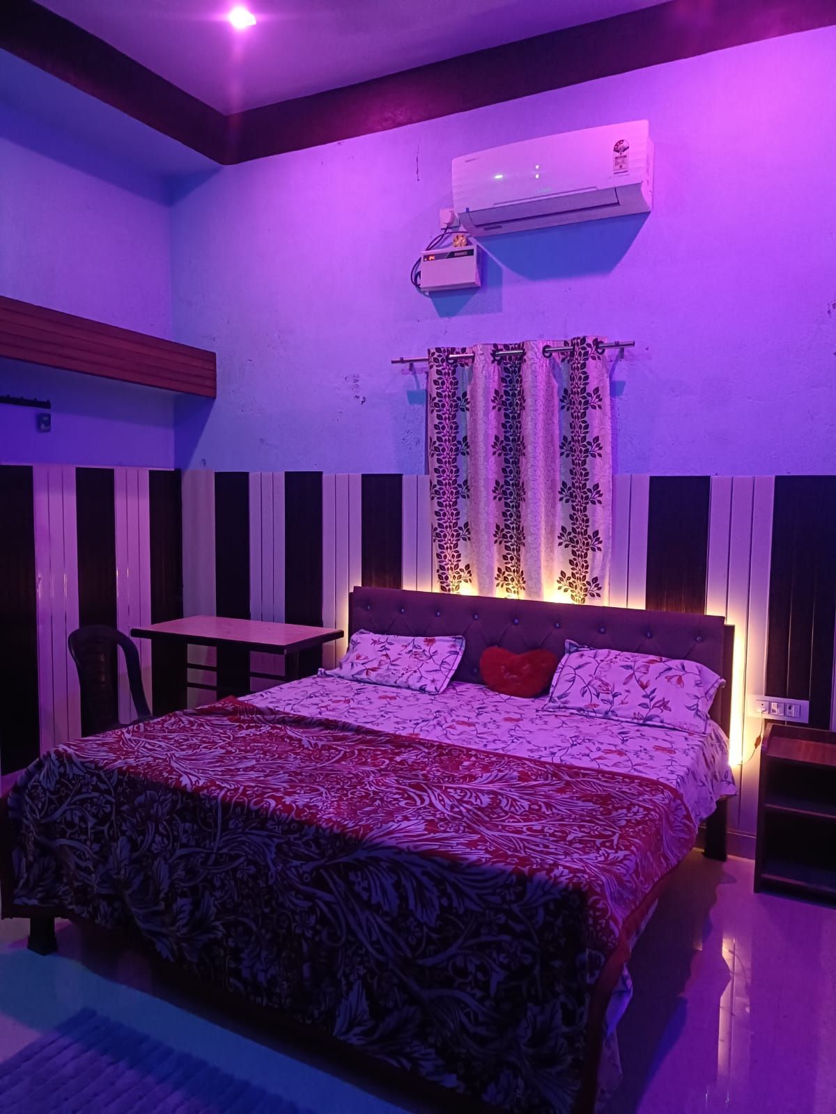A bedroom with a bed, a table, and a chair. There is an air conditioning unit on the wall.
