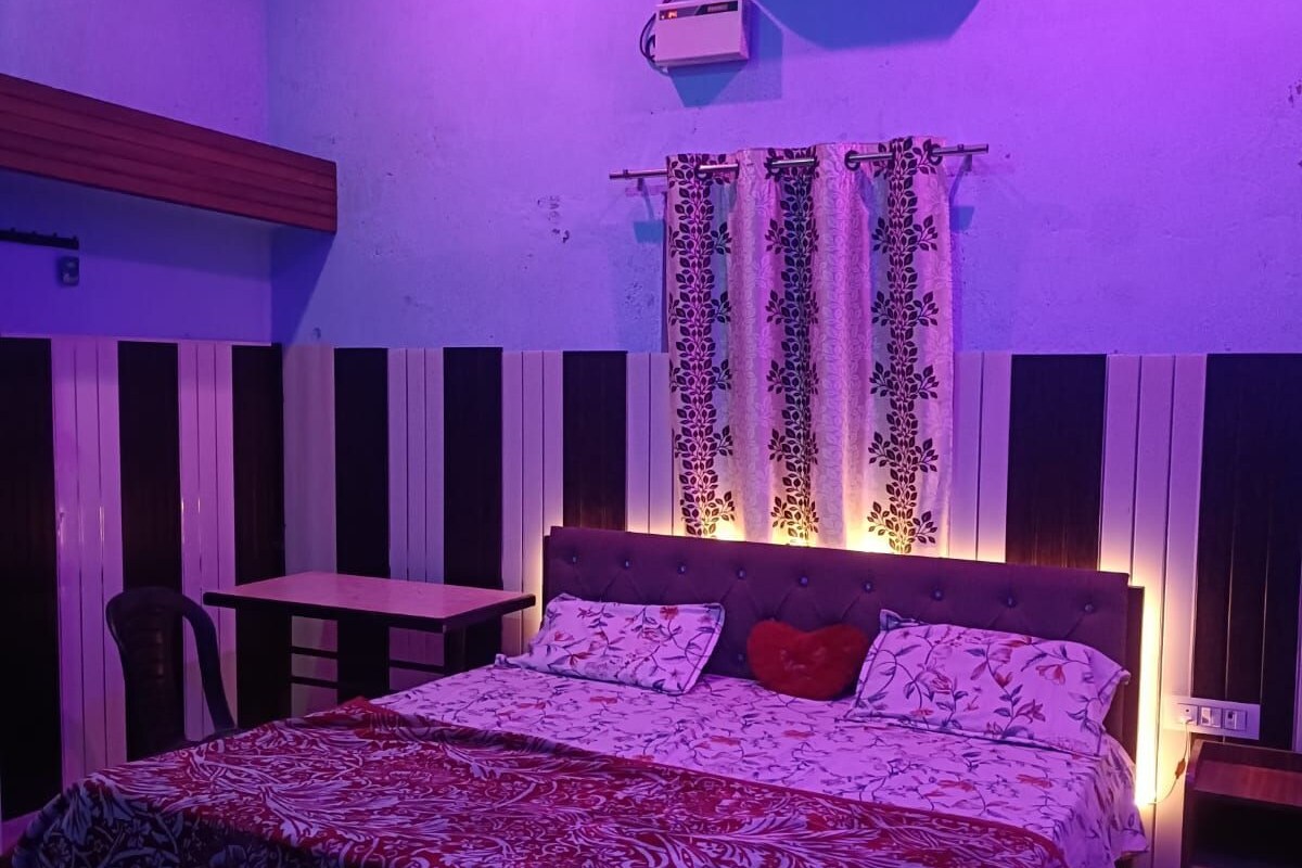 A bedroom with a bed, a table, and a chair. There is an air conditioning unit on the wall.