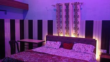 A bedroom with a bed, a table, and a chair. There is an air conditioning unit on the wall.