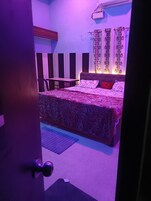Un dormitorio con una cama, una mesita de noche, una silla y una ventana con cortinas.