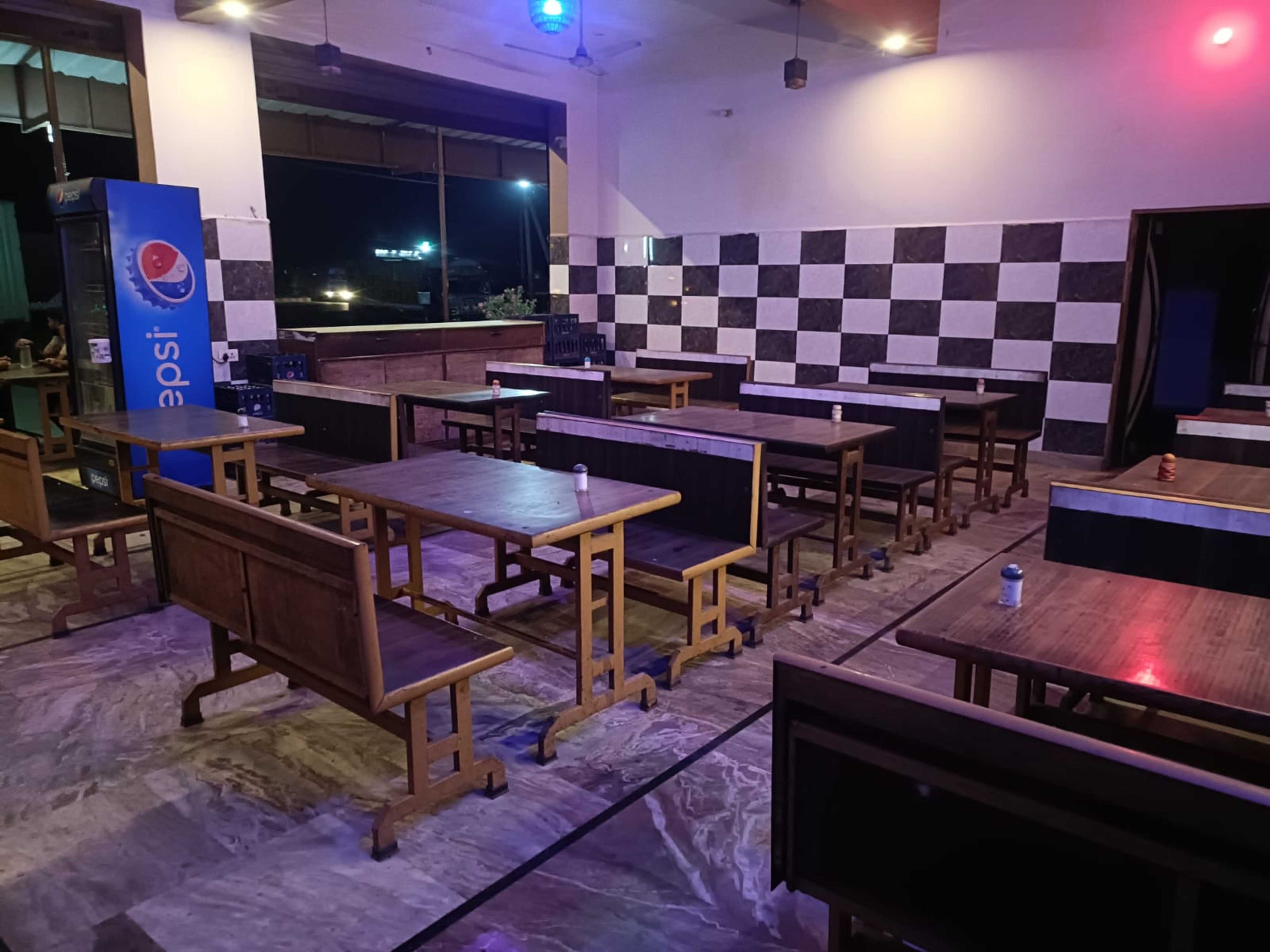 Interior de restaurante con varias mesas y bancos de madera, una máquina expendedora de Pepsi y una pared a cuadros.