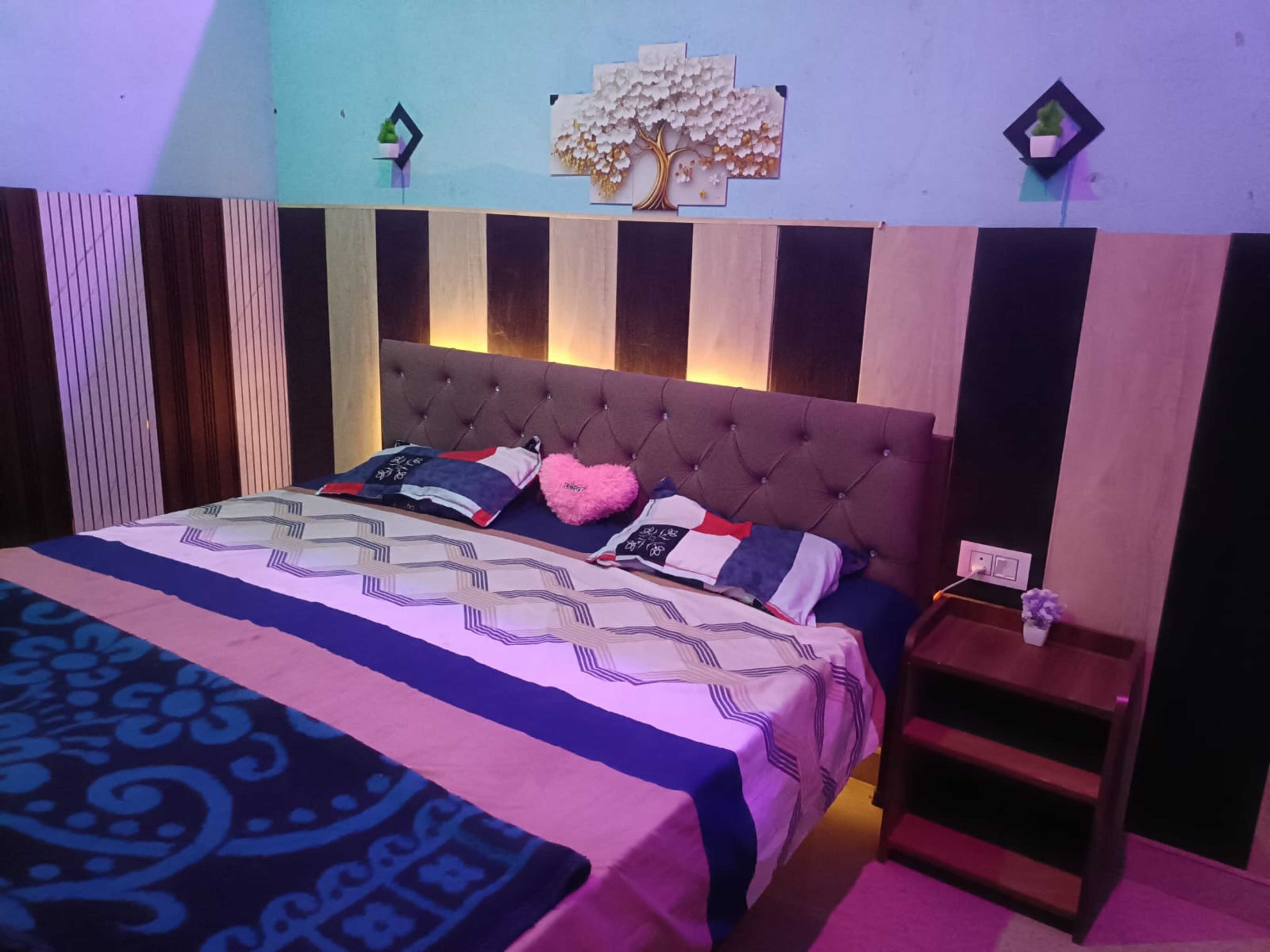 Un dormitorio con cabecera capitonada, colcha estampada y mesita de noche con lámpara.