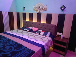 A bedroom with a tufted headboard, a patterned bedspread, and a bedside table with a lamp.