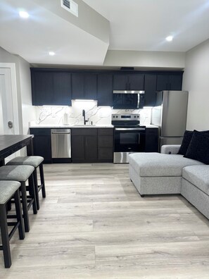 A modern kitchen with dark cabinets, a stainless steel refrigerator, and a built-in oven. - Modern 2 Bedroom Studio Retreat Near Maple-Lawn (Fulton)