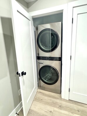 A laundry room with two stacked washing machines, a white door, and a light-colored floor. - Modern 2 Bedroom Studio Retreat Near Maple-Lawn (Fulton)