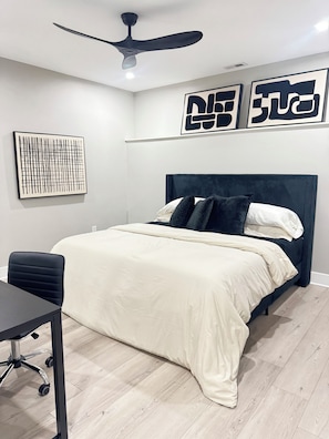 A bedroom with a bed, a desk, a chair, a ceiling fan, and artwork on the wall. - Modern 2 Bedroom Studio Retreat Near Maple-Lawn (Fulton)