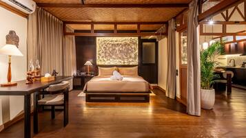 A hotel room with a bed, desk, and chair, a potted plant, and a view of the outside.