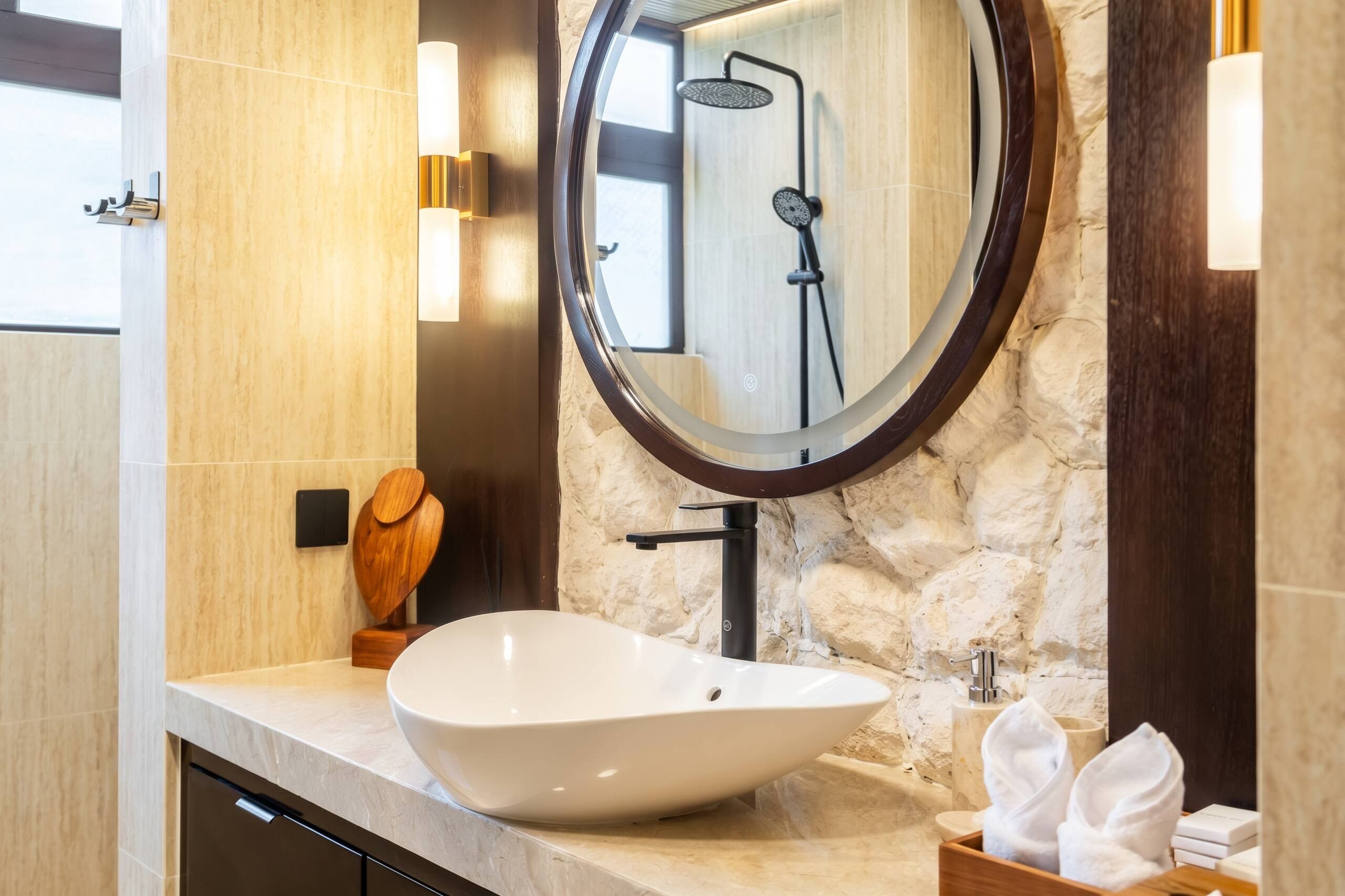 A bathroom with a white vessel sink, a round mirror, and a shower with a handheld showerhead.