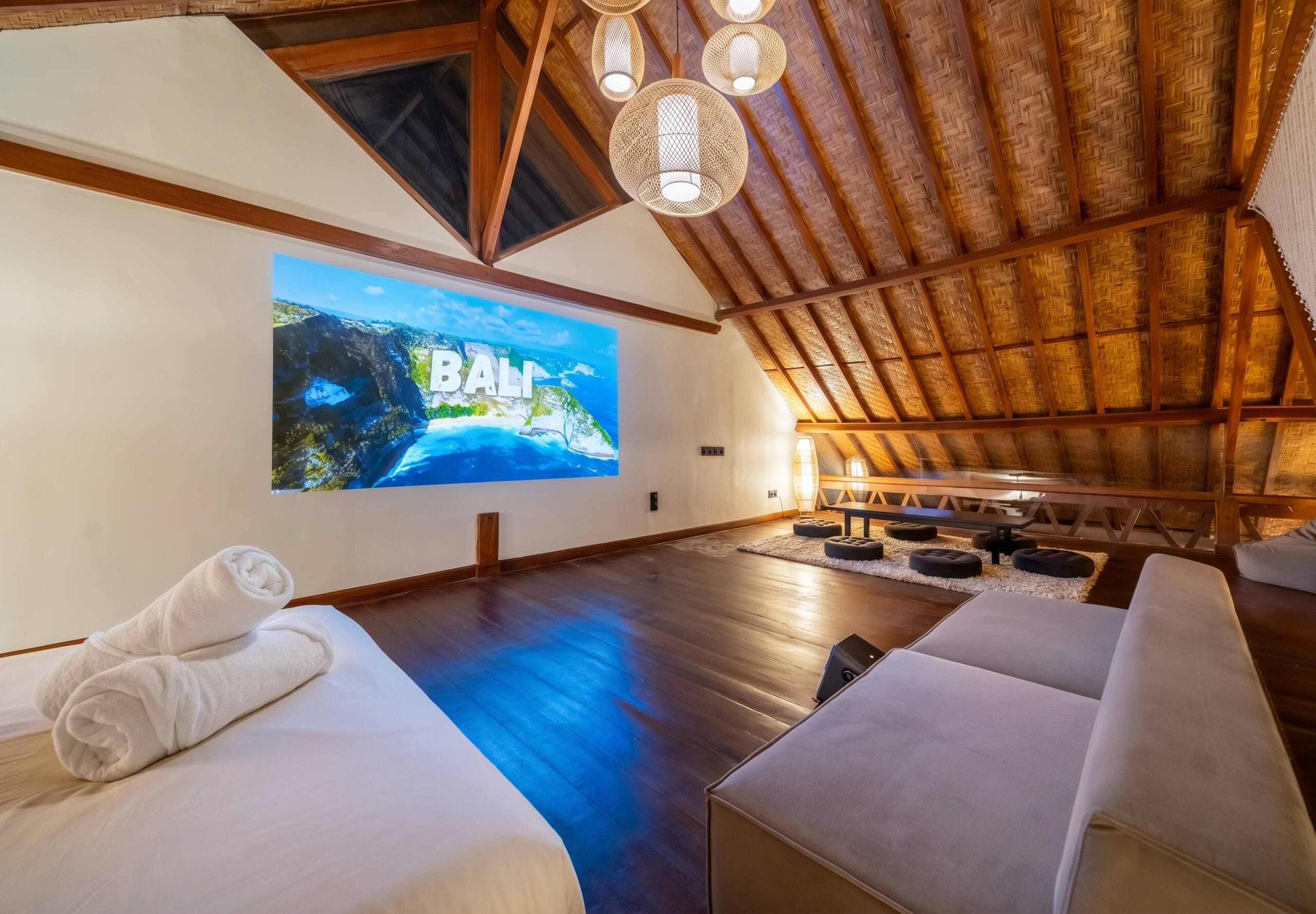 Una habitación amplia con una pantalla grande mostrando una vista panorámica, vigas de madera en el techo y una zona de estar acogedora con cojines.